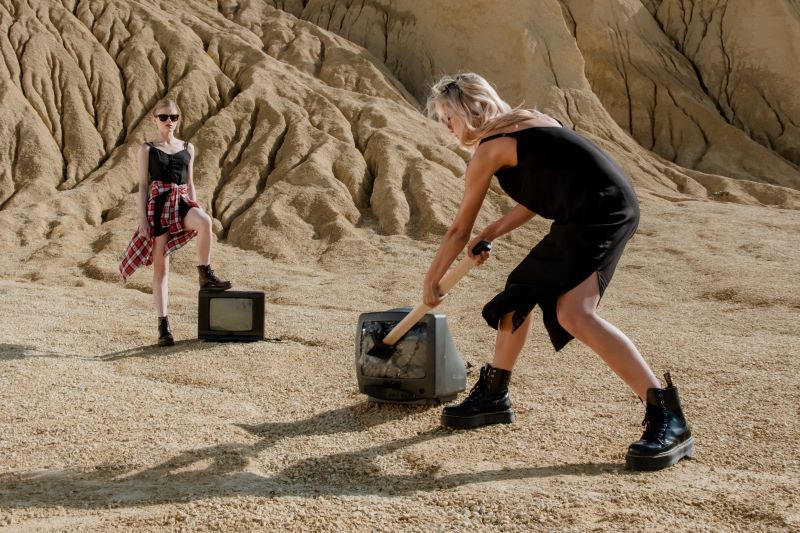 A woman smashes a TV with a sledgehammer in a desert. 